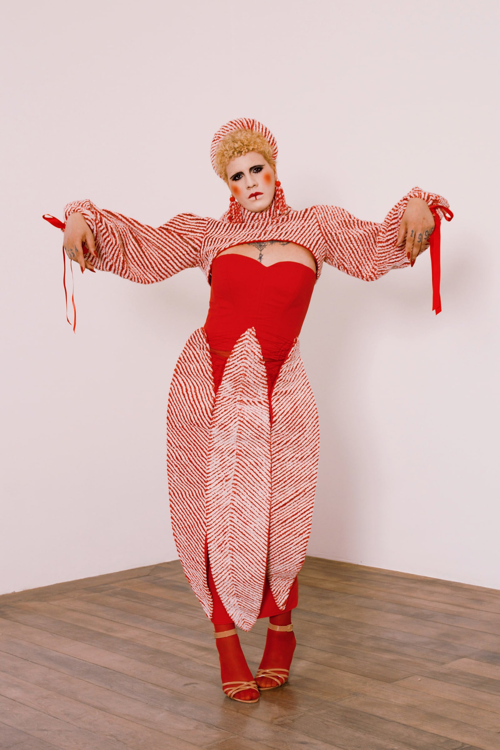 Fotografia de corpo inteiro do look: vestido vermelho ajustado, mangas amplas e painéis alongados de tecido listrado em vermelho e branco.